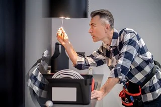 Profile of man touching lamp on kitchen hood Renovation. Profile of concentrated middle aged man in plaid shirt touching screwdriver to lamp on kitchen range hood in modern kitchen at home